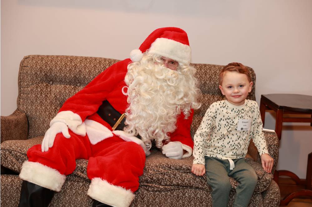 An alums son sitting with Santa on the couch.